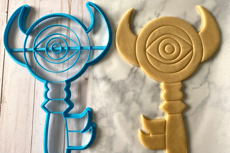 Op de afbeelding: Een blauwe plastic koekjesvormer in de vorm van een sleutel met een oogontwerp en een bruine suikerkoek die met de vormer is uitgestoken.