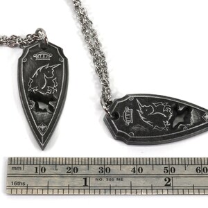 May include: Two silver necklaces with a black pendant shaped like a shield with a unicorn design. The pendant is about 6 cm long.