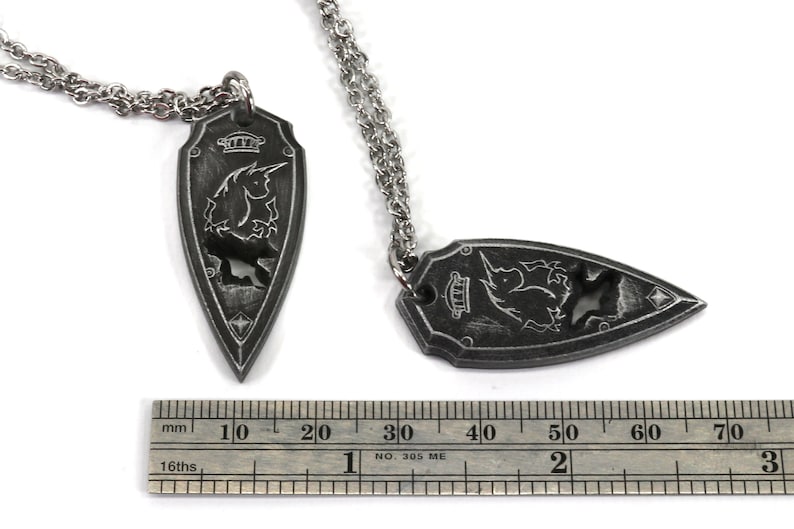 May include: Two silver necklaces with a black pendant shaped like a shield with a unicorn design. The pendant is about 6 cm long.