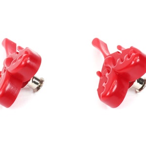 May include: Two red plastic bottle openers with a unique design. The openers have a pointed end and a flat, serrated edge for opening bottles.