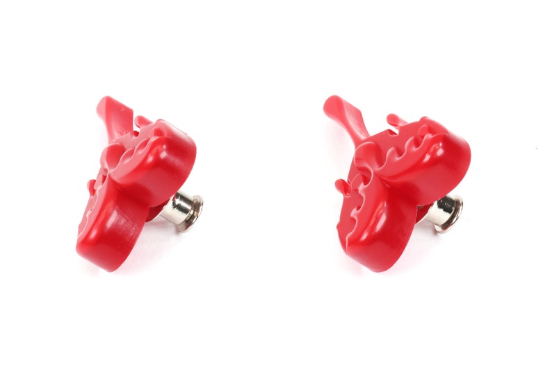 May include: Two red plastic bottle openers with a unique design. The openers have a pointed end and a flat, serrated edge for opening bottles.