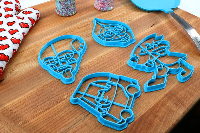 Puede incluir: Cuatro cortadores de galletas de pl&aacute;stico azul con forma de personajes de dibujos animados. Los cortadores est&aacute;n sobre una superficie de madera.