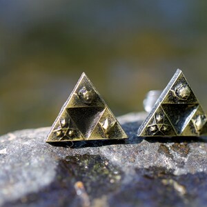May include: A pair of gold-toned earrings shaped like a triangle with a design of a stylized triforce symbol.