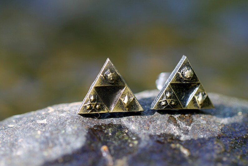 May include: A pair of gold-toned earrings shaped like a triangle with a design of a stylized triforce symbol.