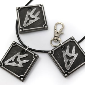 May include: Three silver-toned pendants with a black and silver design. The pendants are attached to a black cord and a silver chain. The pendants are shaped like squares with rounded corners. The design on the pendants is a stylized hand with three fingers.