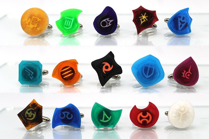 May include: Set of 15 colorful cufflinks featuring various symbols and designs. The cufflinks are made of clear, opaque, and translucent plastic and have a silver metal backing.