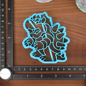 May include: Blue plastic cookie cutter shaped like a cartoon character with spikes on its back.