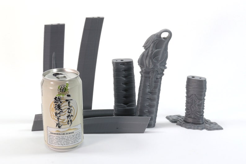 May include: Five 3D printed gray plastic pieces, including a tall, slender piece with a decorative top, a shorter, wider piece with a decorative top, and three rectangular pieces. A can of Japanese beer is in the foreground.