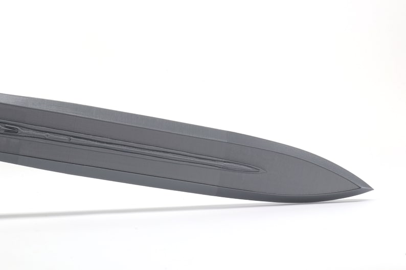 May include: A close-up of the blade of a gray sword. The blade has a textured surface and a sharp point.