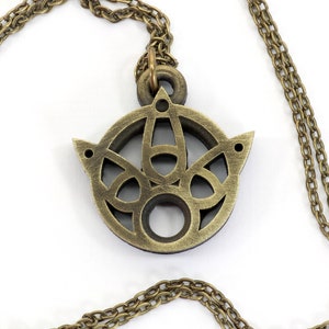 May include: A gold-toned necklace with a circular pendant featuring a detailed, intricate design. The pendant has a cutout pattern and a smooth, polished finish.