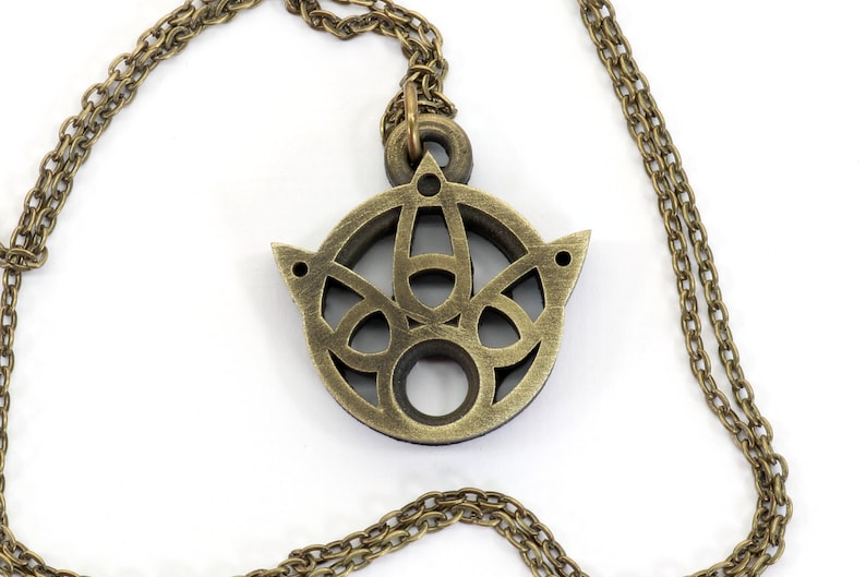 May include: A gold-toned necklace with a circular pendant featuring a detailed, intricate design. The pendant has a cutout pattern and a smooth, polished finish.
