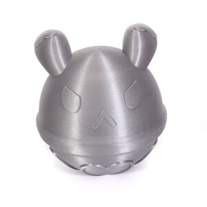 Op de afbeelding: Een zilverkleurig, 3D-geprint speelgoed met een afgeronde vorm en twee kleine oren. Het speelgoed heeft een gezicht met twee ogen en een kleine mond.