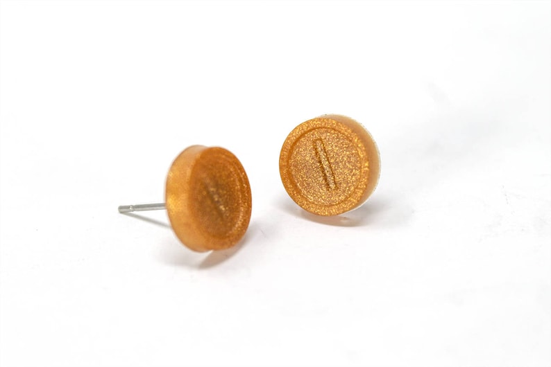 May include: A pair of gold-colored stud earrings with a textured surface. Each earring features a raised, horizontal line.