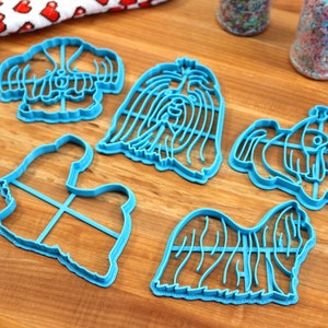 May include: Five blue plastic cookie cutters shaped like Shih Tzu dogs. The cutters are on a wooden surface.