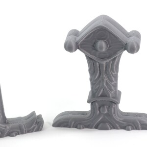 May include: A gray 3D printed model of a Viking axe head with a detailed handle and a decorative top. The axe head is designed with a textured surface and a raised design on the top.