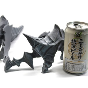 May include: Two grey 3D printed sculptures resembling claws or horns, with a can of Japanese beer in the background. The can is white with black text that reads "Koshihikari ECHIGO" and "越後こしひかり" in Japanese.