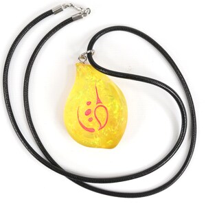 May include: A yellow teardrop-shaped pendant with a red symbol on a black cord necklace.