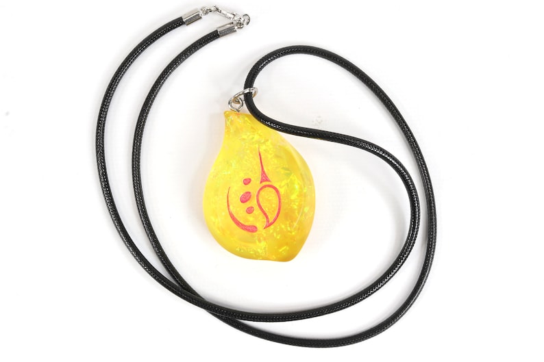May include: A yellow teardrop-shaped pendant with a red symbol on a black cord necklace.