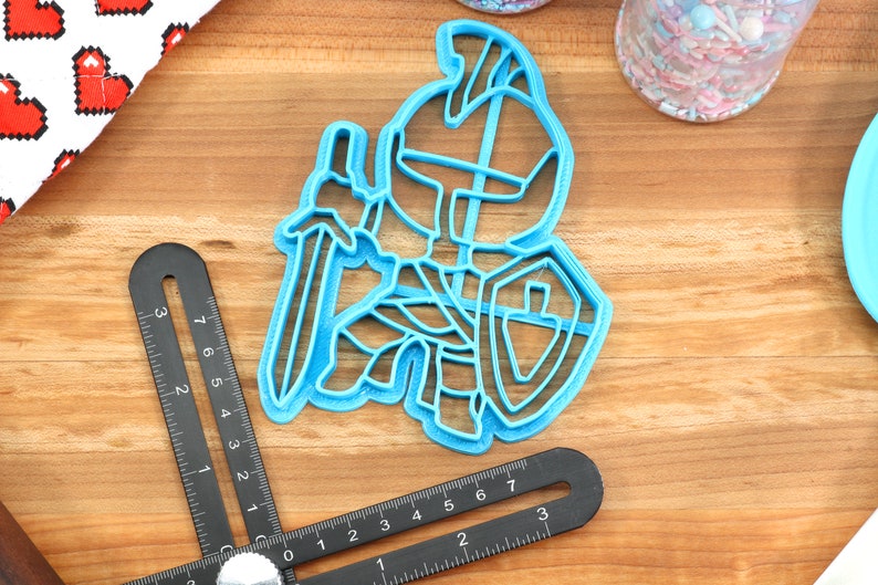 May include: Blue plastic cookie cutter shaped like a knight holding a sword and shield.