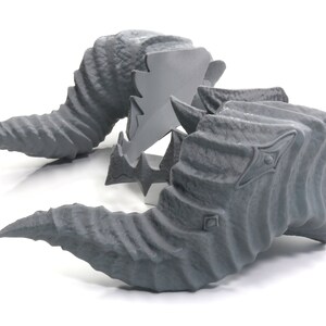 May include: Two gray, textured, 3D printed horns. The horns are curved and have a pointed tip. They are designed to look like a mythical creature's horns.