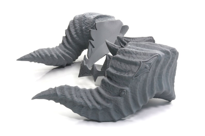 May include: Two gray, textured, 3D printed horns. The horns are curved and have a pointed tip. They are designed to look like a mythical creature's horns.