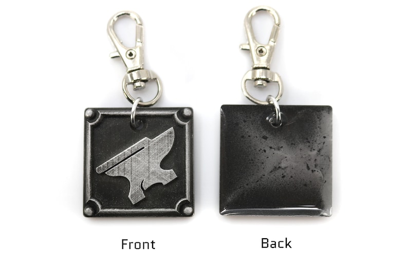 May include: A silver metal keychain with a square charm. The front of the charm features a silver anvil design. The back of the charm is plain and silver.