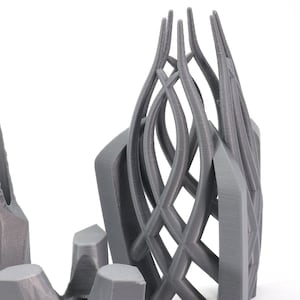 May include: Two 3D printed sculptures, one with a geometric, spiky design and the other with a more organic, flowing design. Both sculptures are made of a gray plastic material.