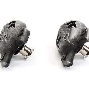 Op de afbeelding: Twee zwarte metalen drukknopen met een decoratief ontwerp. De drukknopen hebben een zilveren metalen pen.