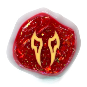 May include: A red resin cabochon with a yellow flame design. The cabochon is set in a clear resin base.