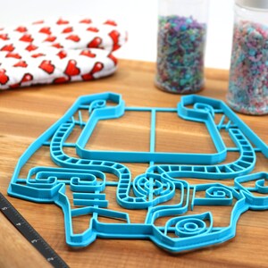 Peut inclure: Un emporte-pi&egrave;ce en plastique bleu en forme de voiture. L'emporte-pi&egrave;ce est sur une surface en bois avec un rouleau &agrave; p&acirc;tisserie et deux pots de vermicelles.
