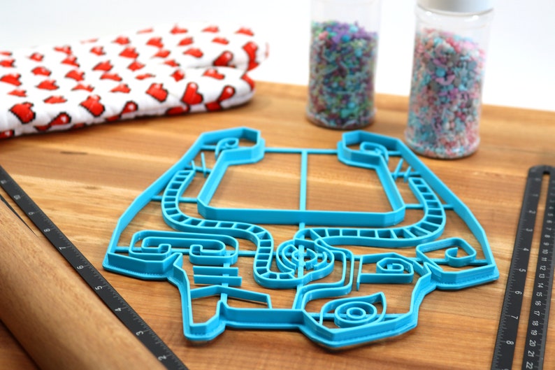 Peut inclure: Un emporte-pi&egrave;ce en plastique bleu en forme de voiture. L'emporte-pi&egrave;ce est sur une surface en bois avec un rouleau &agrave; p&acirc;tisserie et deux pots de vermicelles.