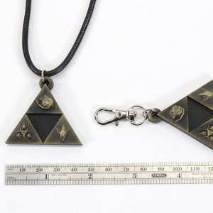 May include: A gold-colored pendant necklace and keychain featuring a triangular design with four symbols. The necklace has a black cord and the keychain has a silver metal clasp.