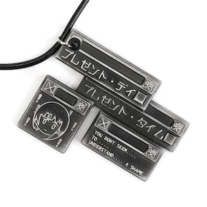 May include: A silver necklace with a pendant featuring a series of stacked rectangular metal tags. The tags have Japanese text that reads "プレゼント・ディロ" and "プレゼント・タイム" and English text that reads "YOU DONT SEEM... TO UNDERSTAND... A SHAME".