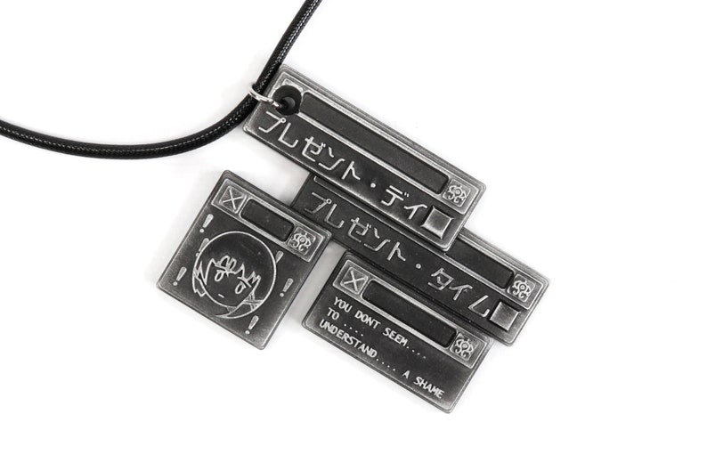 May include: A silver necklace with a pendant featuring a series of stacked rectangular metal tags. The tags have Japanese text that reads "プレゼント・ディロ" and "プレゼント・タイム" and English text that reads "YOU DONT SEEM... TO UNDERSTAND... A SHAME".