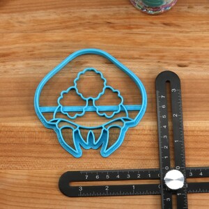 May include: Blue plastic cookie cutter shaped like a mushroom with three white mushroom caps on top. The cookie cutter is 2 inches wide and 2.5 inches tall.