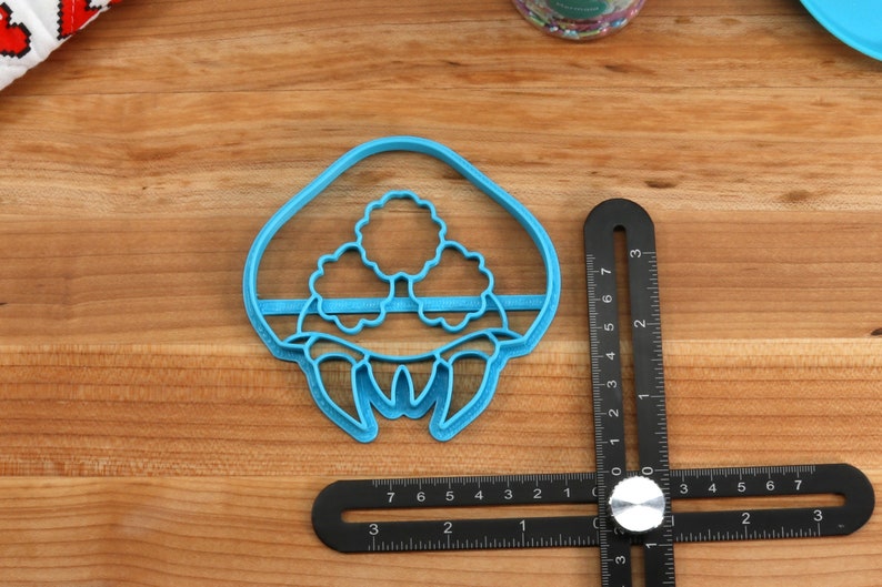 May include: Blue plastic cookie cutter shaped like a mushroom with three white mushroom caps on top. The cookie cutter is 2 inches wide and 2.5 inches tall.