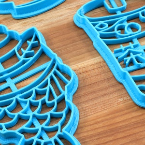 May include: Several light blue plastic cookie cutters in various shapes, including a fish and a beverage cup with Chinese characters. The cutters are on a wooden surface.