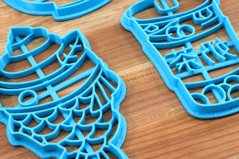 May include: Several light blue plastic cookie cutters in various shapes, including a fish and a beverage cup with Chinese characters. The cutters are on a wooden surface.