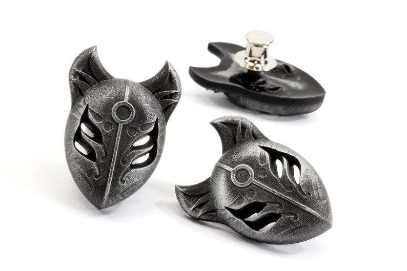 Op de afbeelding: Drie zilverkleurige metalen vossenmasker-spelden. De maskers hebben ingewikkelde details en een textuur. De spelden zijn ontworpen om op kleding of tassen te worden gedragen.