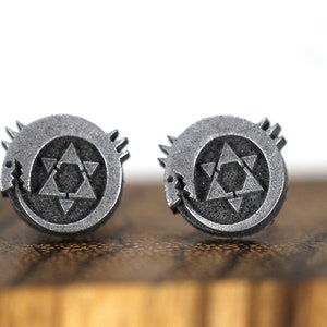 May include: A pair of silver earrings featuring a circular design with a stylized star of David inside a circle with a snake-like creature wrapping around it.