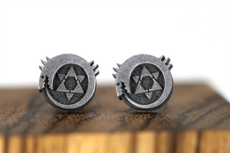 May include: A pair of silver earrings featuring a circular design with a stylized star of David inside a circle with a snake-like creature wrapping around it.
