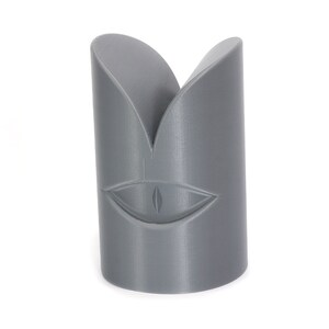 May include: A grey 3D printed object shaped like a face with a single eye in the centre.
