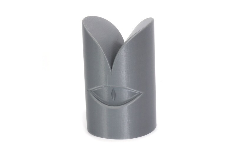 May include: A grey 3D printed object shaped like a face with a single eye in the centre.