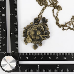 May include: A bronze steampunk-style necklace with a circular pendant featuring gears, cogs, and a face. The pendant is about 2 inches in diameter.