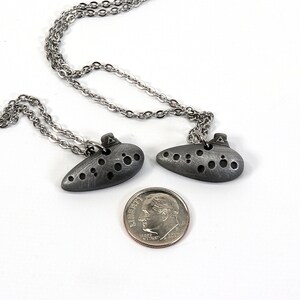 May include: Two silver ocarina necklaces with a silver chain. The ocarinas are about the size of a US dime.