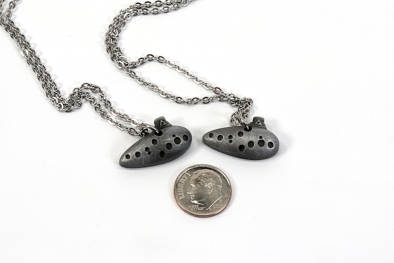 May include: Two silver ocarina necklaces with a silver chain. The ocarinas are about the size of a US dime.