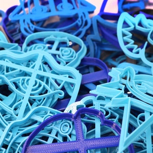 Op de afbeelding: Een close-up van een stapel blauwe en paarse plastic koekjesvormen. De vormen zijn in de vorm van verschillende nautische thema's, waaronder ankers, schepen en zeedieren.