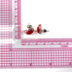 Puede incluir: Un par de pendientes de bot&oacute;n de resina roja y transparente con postes de plata. Los pendientes miden aproximadamente 1 cm de di&aacute;metro.