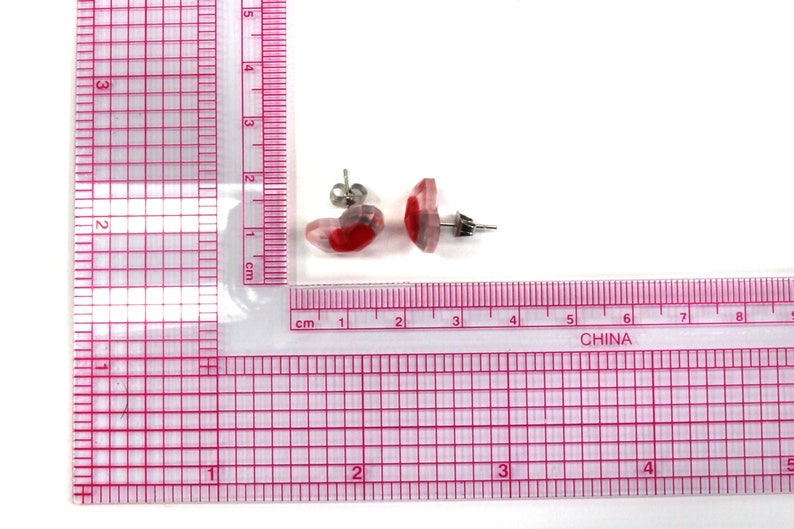 Puede incluir: Un par de pendientes de bot&oacute;n de resina roja y transparente con postes de plata. Los pendientes miden aproximadamente 1 cm de di&aacute;metro.