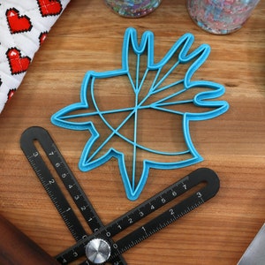 May include: A blue plastic cookie cutter shaped like a starburst with multiple points. The cutter is on a wooden surface with a ruler and a rolling pin.
